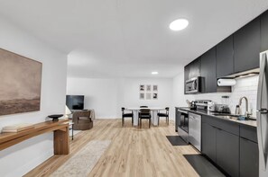 Een moderne keuken met donkere kastjes, een roestvrijstalen koelkast en een eethoek met een tafel en stoelen.