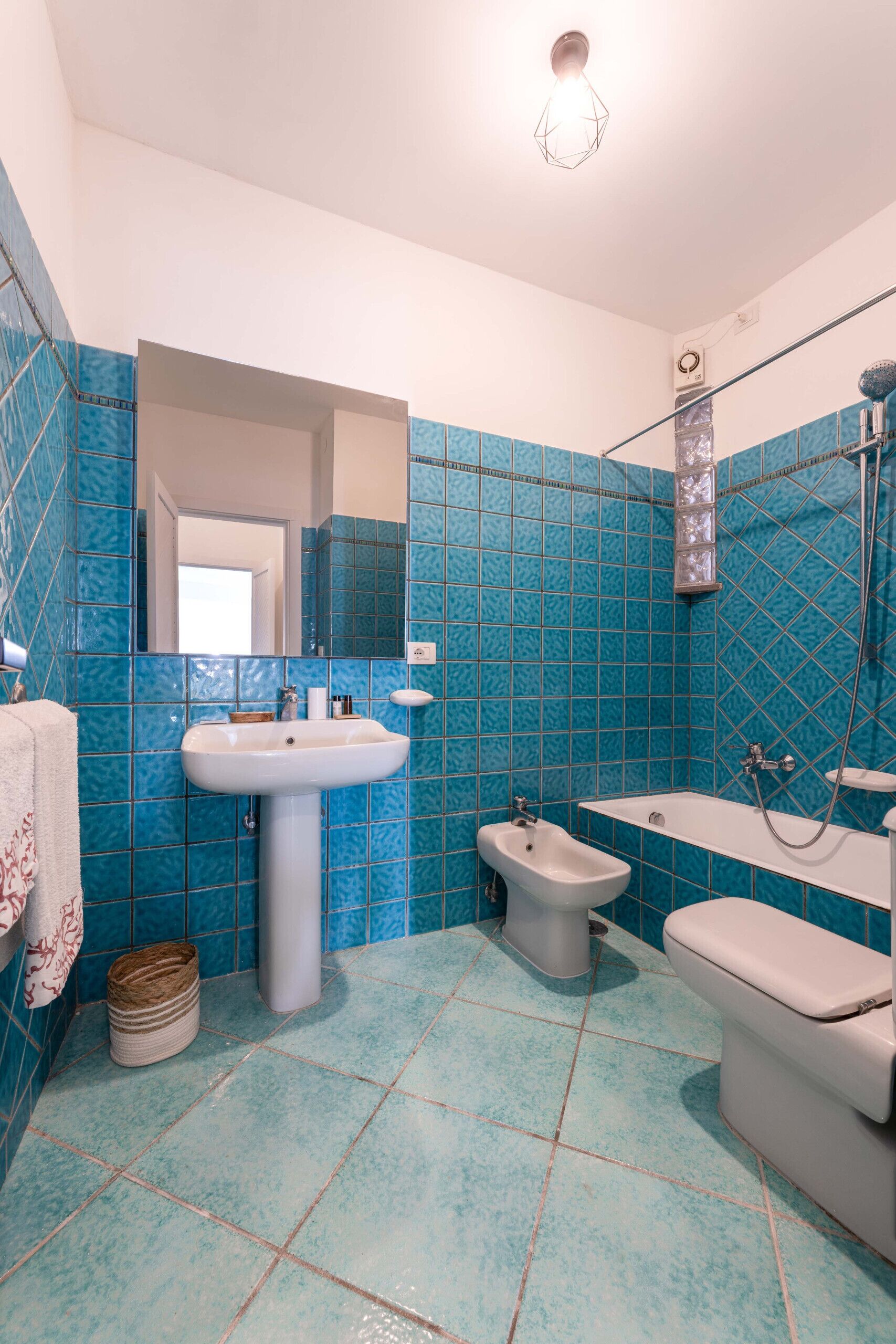 A bathroom with blue tiles, a sink, a bidet, a toilet, and a shower.