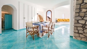 A dining area with a table set for four, surrounded by white walls and a stone accent wall. - Villa La Torre in Massa Lubrense (Massa Lubrense)