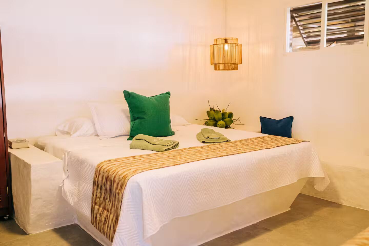 A neatly made bed with white linens, a green pillow, a blue pillow, and a woven throw blanket.