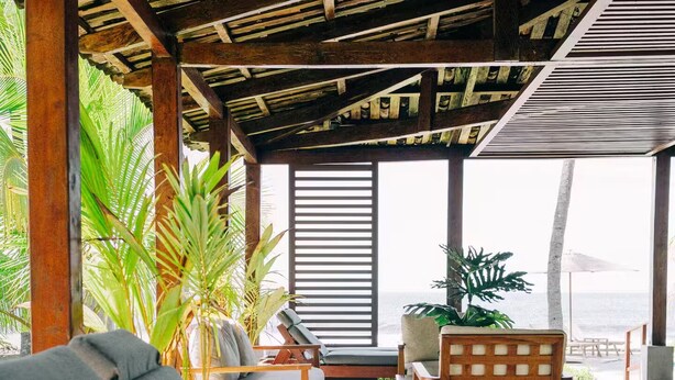 A covered outdoor seating area with wooden furniture and tropical plants. - La Perla @ Rocamar (Jicalapa)