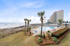 A hotel with a pool area, beach view, and a tall building in the background. - Seaside Beach & Racquet 3205 (Orange Beach)