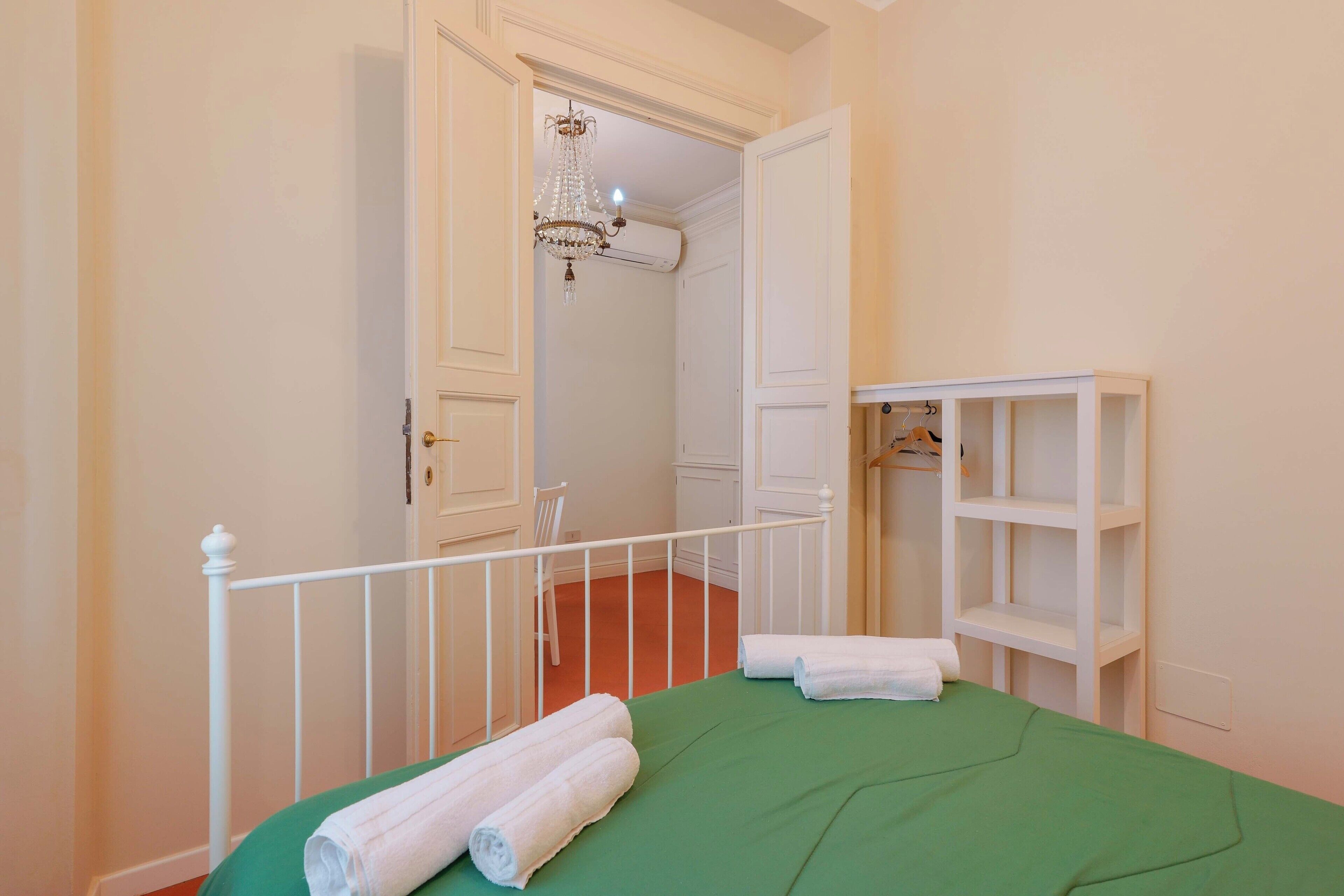 Ein Schlafzimmer mit einer grünen Tagesdecke, weißen Handtüchern, einem weißen Kleiderschrank und einem Kronleuchter im Flur.