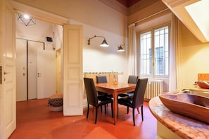 Uma área de refeições com mesa de madeira, quatro cadeiras e iluminação pendente.
