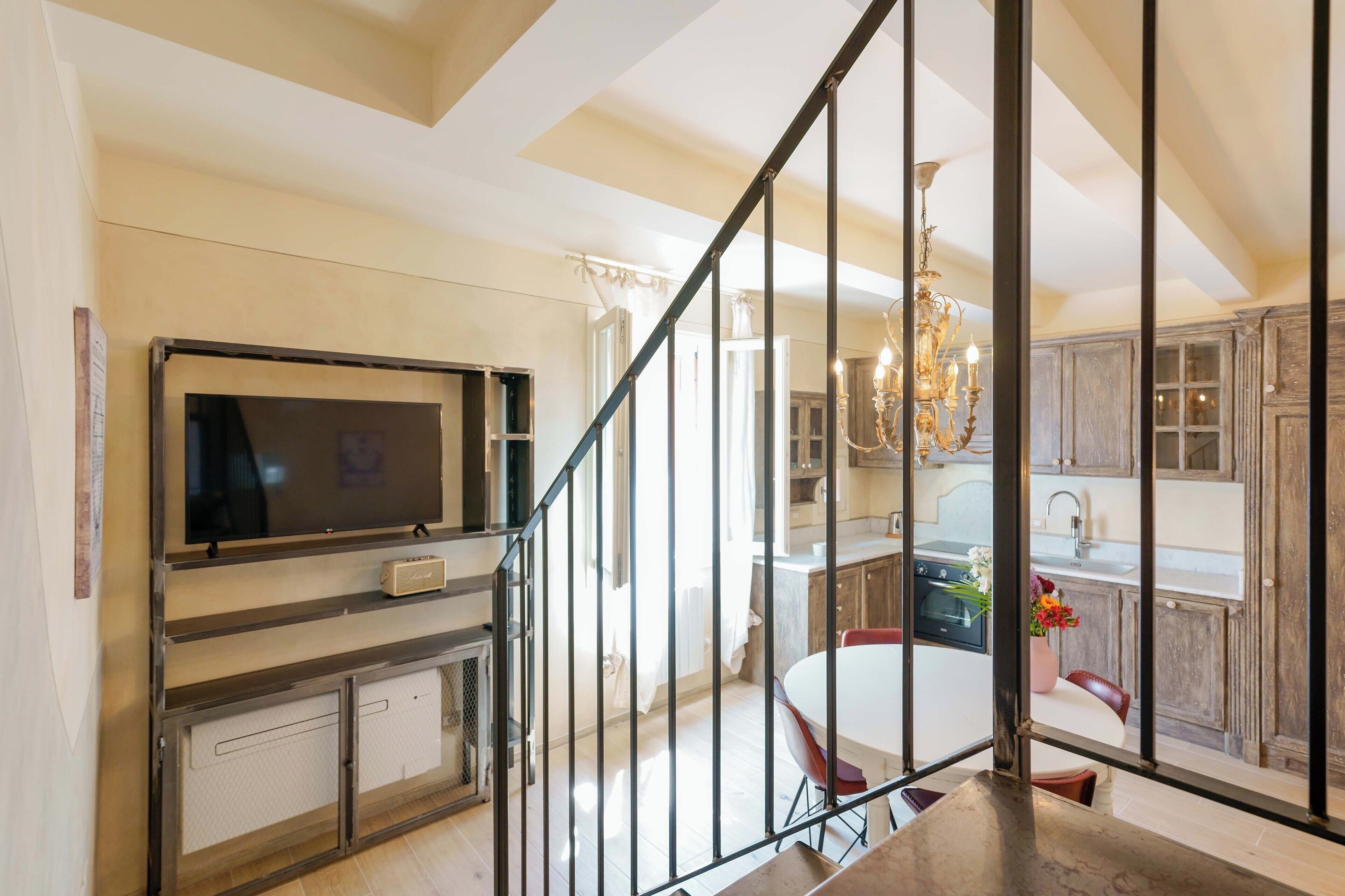 A modern kitchen with a large TV, a dining table, and a chandelier.