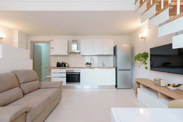 A modern kitchen with white cabinets, a built-in oven, and a stainless steel refrigerator.