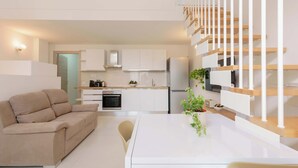 A modern living space with a sofa, dining table, kitchen, and a staircase. - Casarossoblu- Zona Stadio (Bologna)