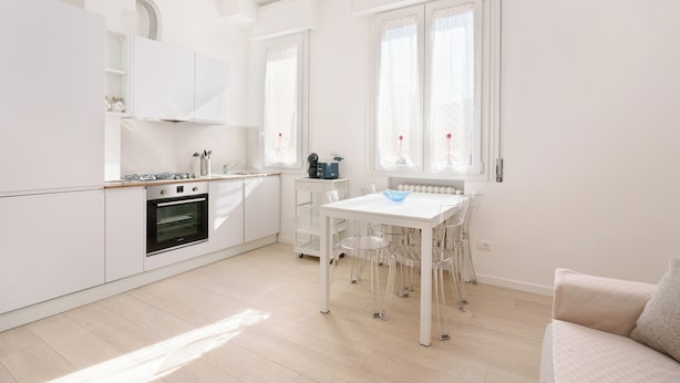 A modern kitchen with white cabinets, a built-in oven, and a dining table with chairs. - Cignani Loft (Bologna)