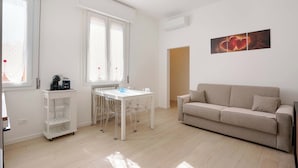 A modern living room with a beige sofa, a white dining table with chairs, and a coffee machine on a white cart. - Cignani Loft (Bologna)