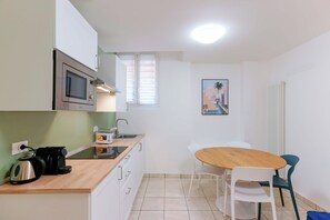 Une cuisine compacte équipée d’un four à micro-ondes, d’une bouilloire et d’un grille-pain, une petite table à manger avec des chaises, et un tableau accroché au mur.