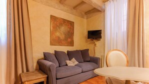 A living room with a sofa, a small table, a chair, a television, and a painting on the wall. - Gallery Guesthouse (Bologna)