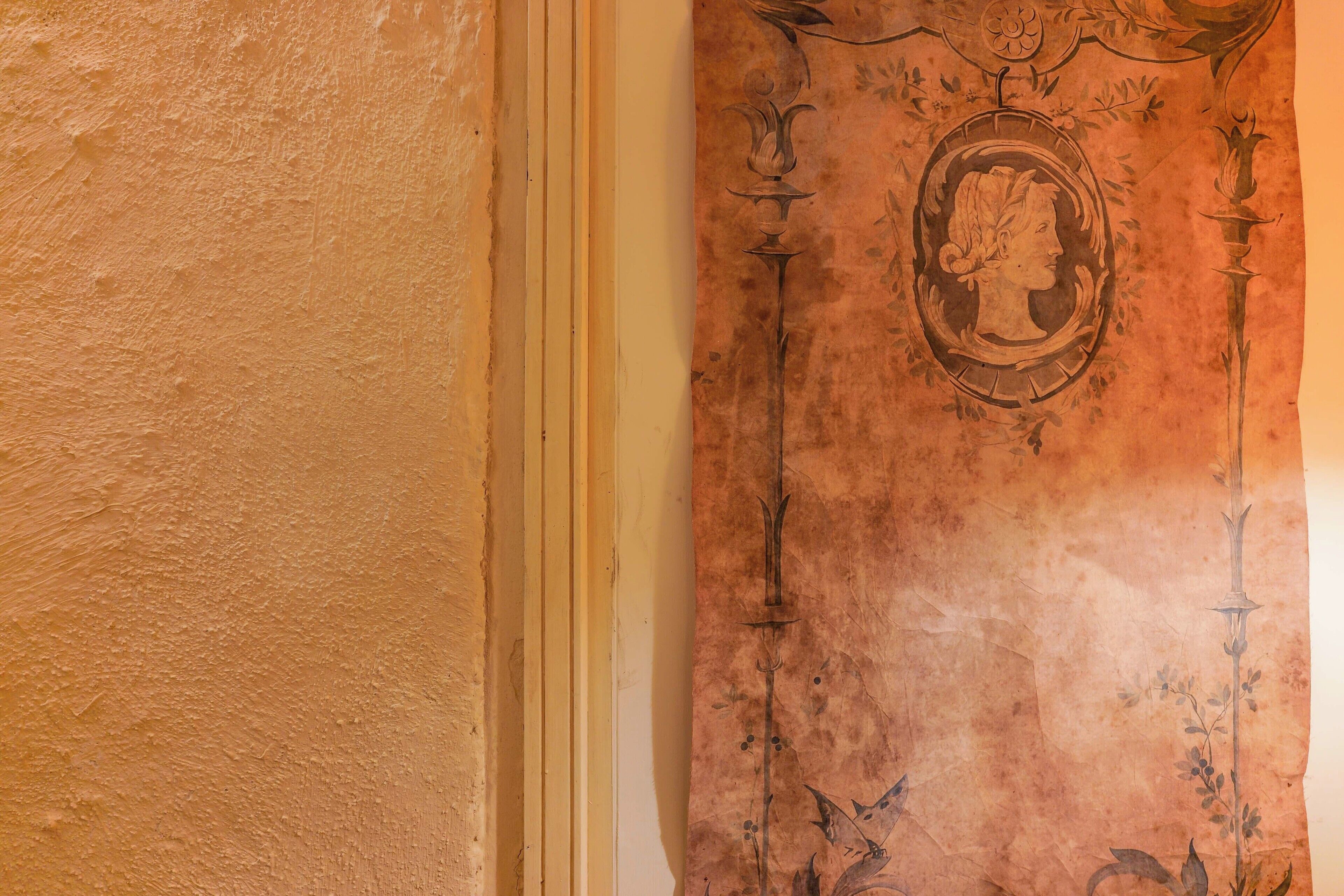 Pared texturizada con un panel decorativo que presenta un marco oval central con un retrato de perfil y follaje circundante.