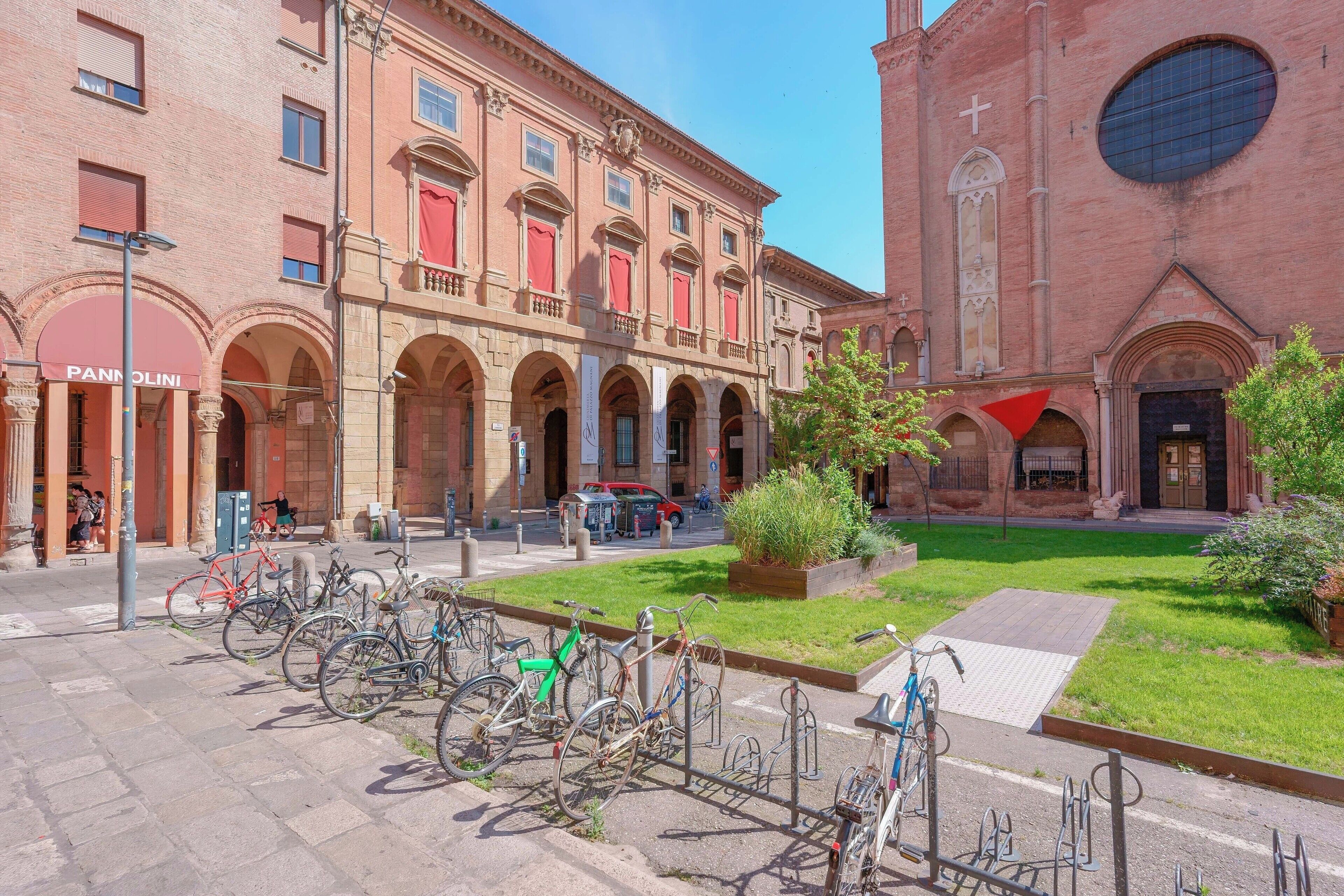 A courtyard with bicycles parked in front of a building with arched windows and a large circular window on the right.