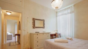 A hotel room with a large bed, a dresser, a mirror, and a chandelier. - Guasto Apartments (Bologna)