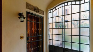 A curved window with a grid pattern, a wooden door with a metal gate, and a wall-mounted light fixture. - Guasto Apartments (Bologna)
