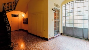 A hallway with a staircase, a door with a metal gate, and a large window. - Guasto Apartments (Bologna)