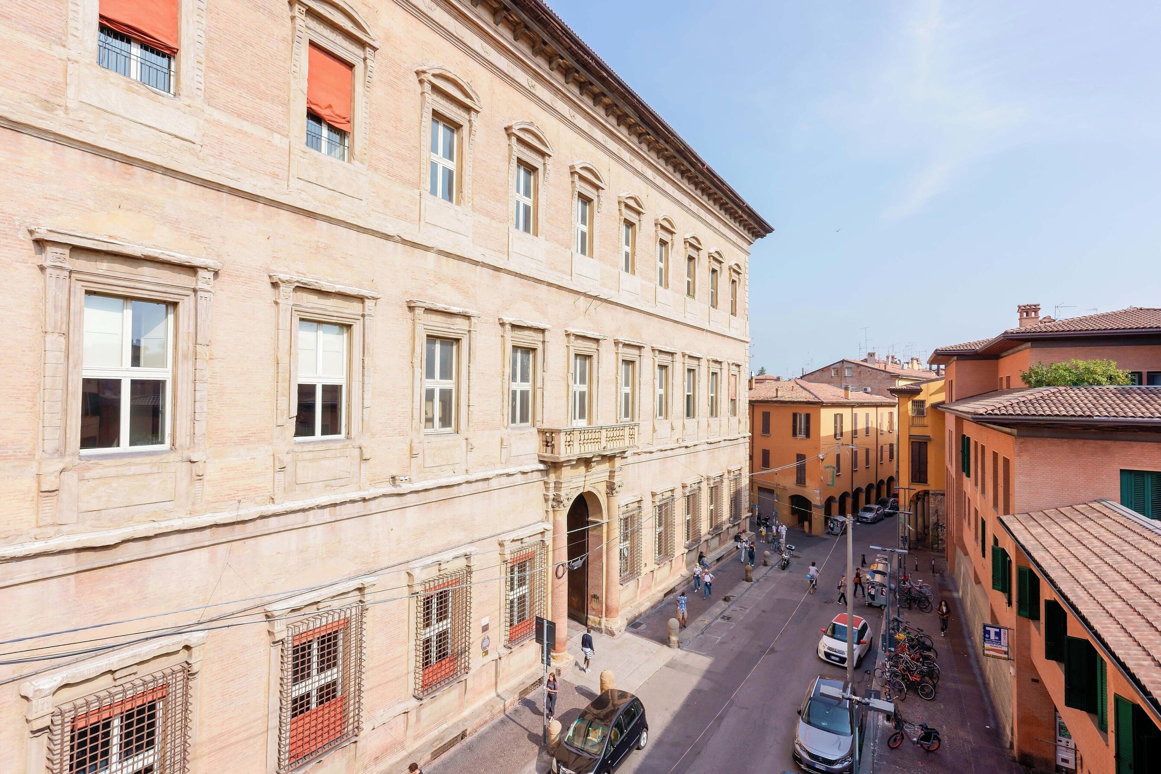 A historic building with a central archway, a street with parked cars and bicycles, and a clear sky.