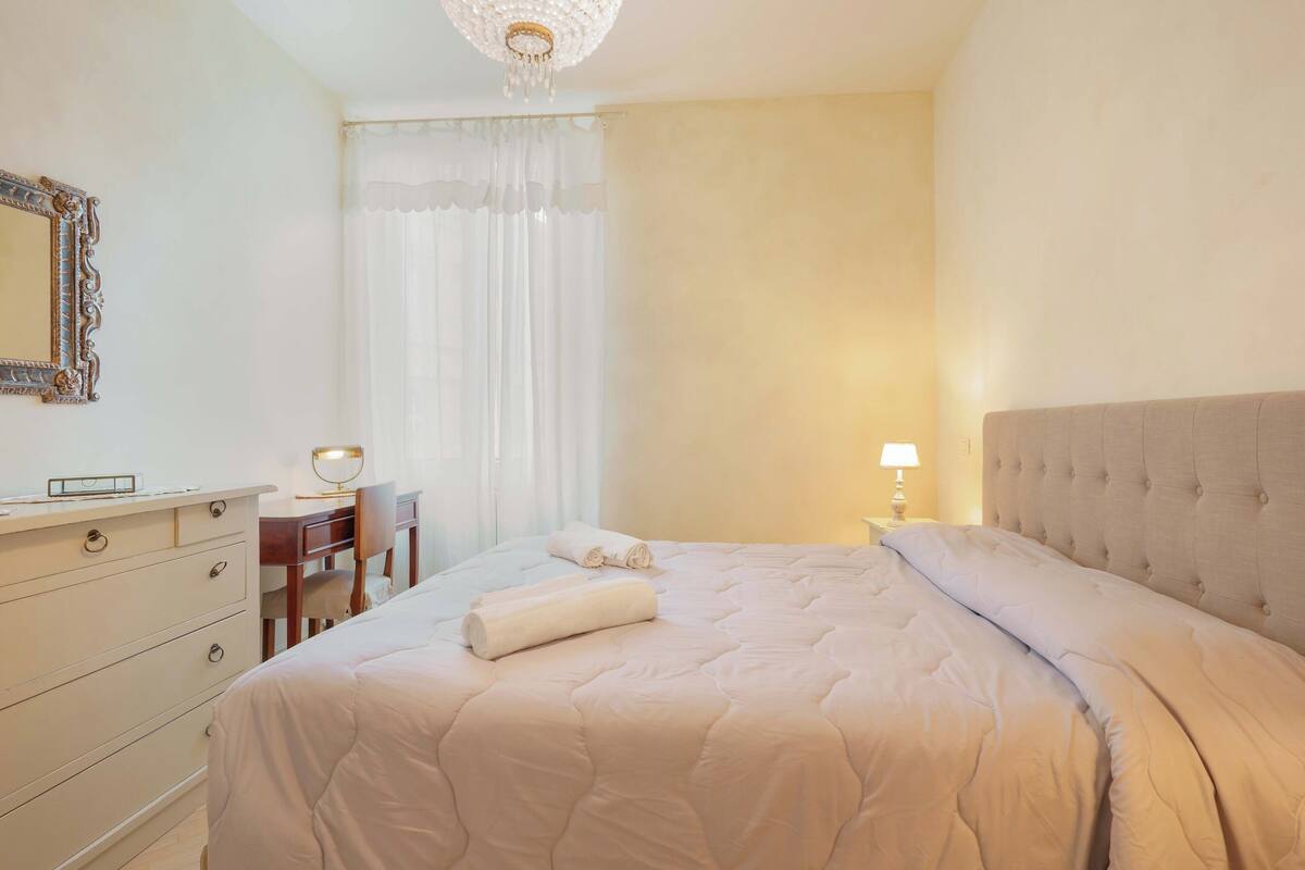 A neatly arranged hotel room with a bed, a desk, a chair, a dresser, and a mirror.