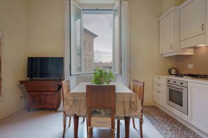 Un coin repas avec une table dressée pour quatre personnes, un téléviseur et une vue sur les bâtiments par la fenêtre.