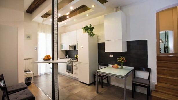A modern kitchen with white cabinets, a central island, and a dining area with two chairs. - Guasto Apartments (Bologna)