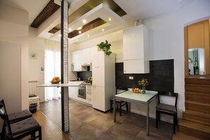A modern kitchen with white cabinets, a central island, and a dining area with two chairs. - Guasto Apartments (Bologna)