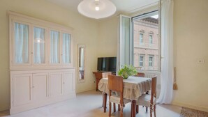 A dining area with a table set for four, a television, and a view of a building through a window. - Guasto Apartments (Bologna)