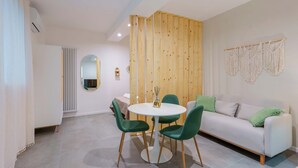 A modern living room with a round dining table, green chairs, a white sofa, and a wooden partition. - Levante Collection (Bologna)