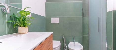 A bathroom with a shower, toilet, bidet, and a potted plant on the sink.