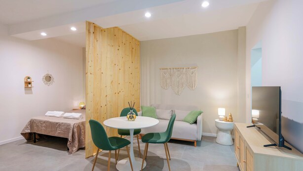 A modern room with a bed, a dining table with chairs, a sofa, a TV, and a small side table. - Levante Collection (Bologna)