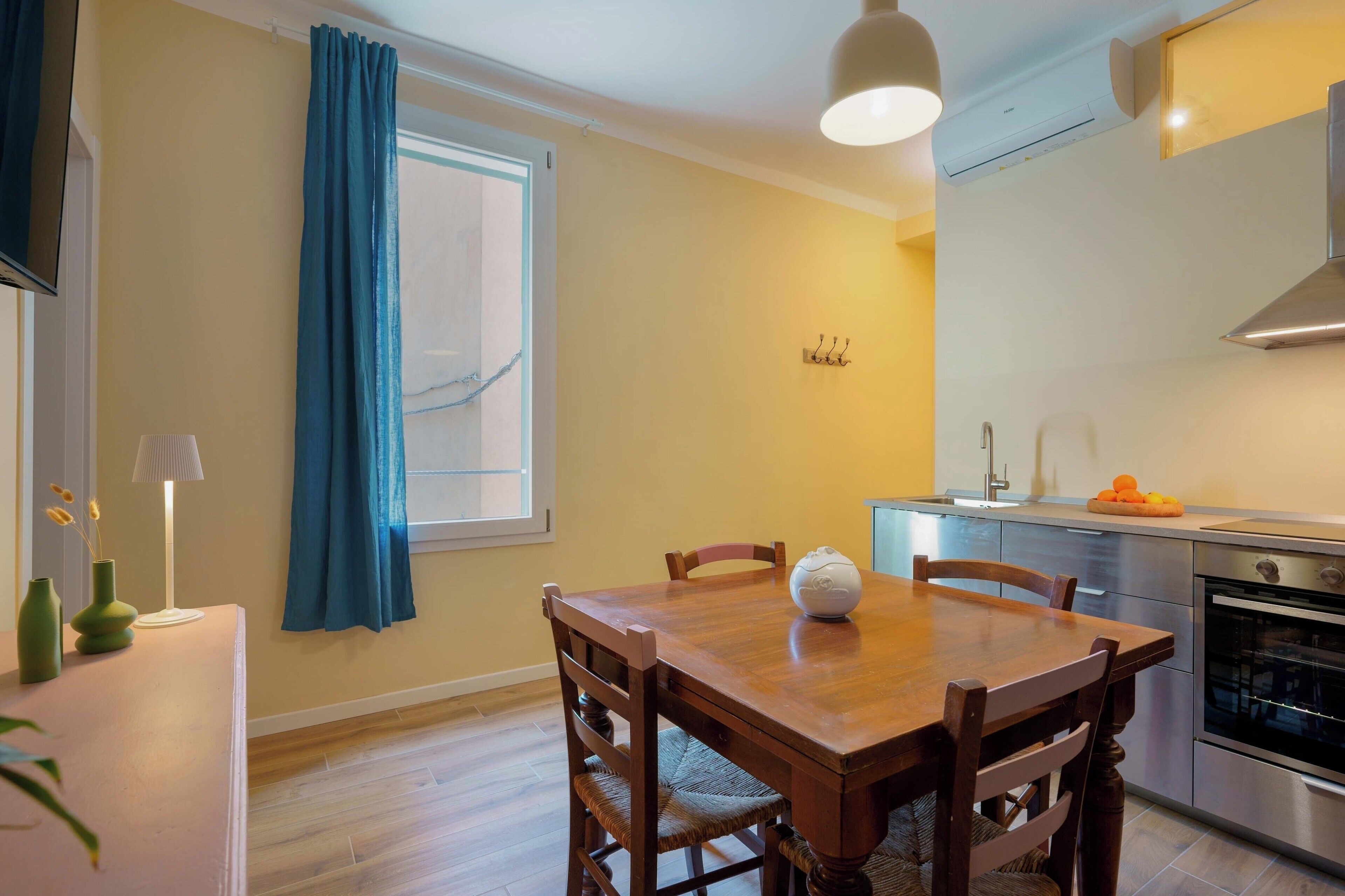 Een eetgedeelte met een houten tafel, stoelen, een lamp en een raam met blauwe gordijnen.