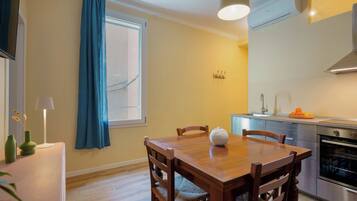 Een eetgedeelte met een houten tafel, stoelen, een lamp en een raam met blauwe gordijnen.
