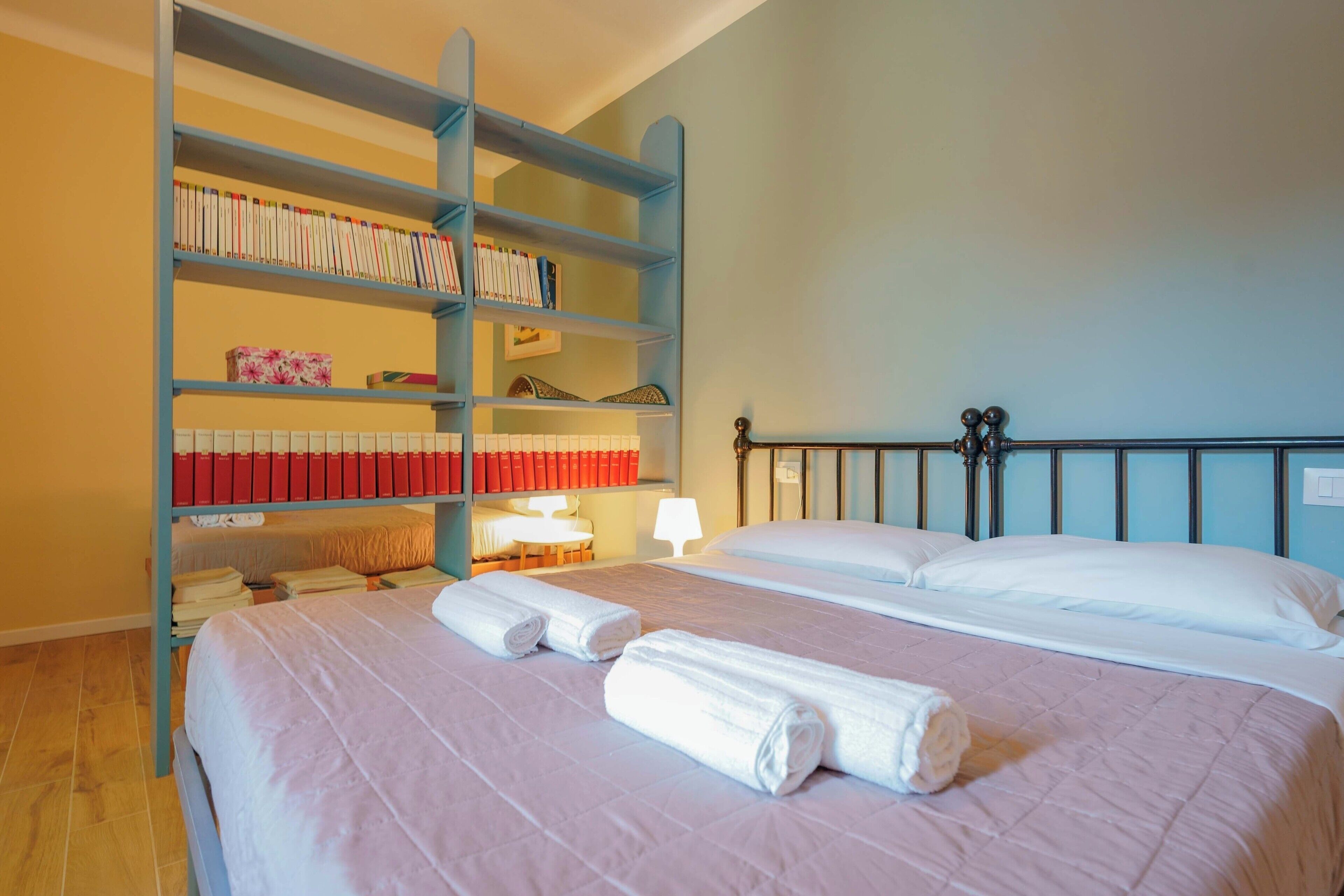 Quarto de hotel com uma cama, uma estante de livros e uma mesa com abajur.