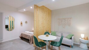 A modern bedroom with a bed, a round dining table with chairs, a white sofa, and a small bedside table with a lamp. - Levante Collection (Bologna)