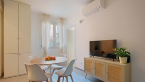 A dining area with a round table, white chairs, a TV on a wooden cabinet, and a potted plant. - Mascarella Apartments (Bologna)