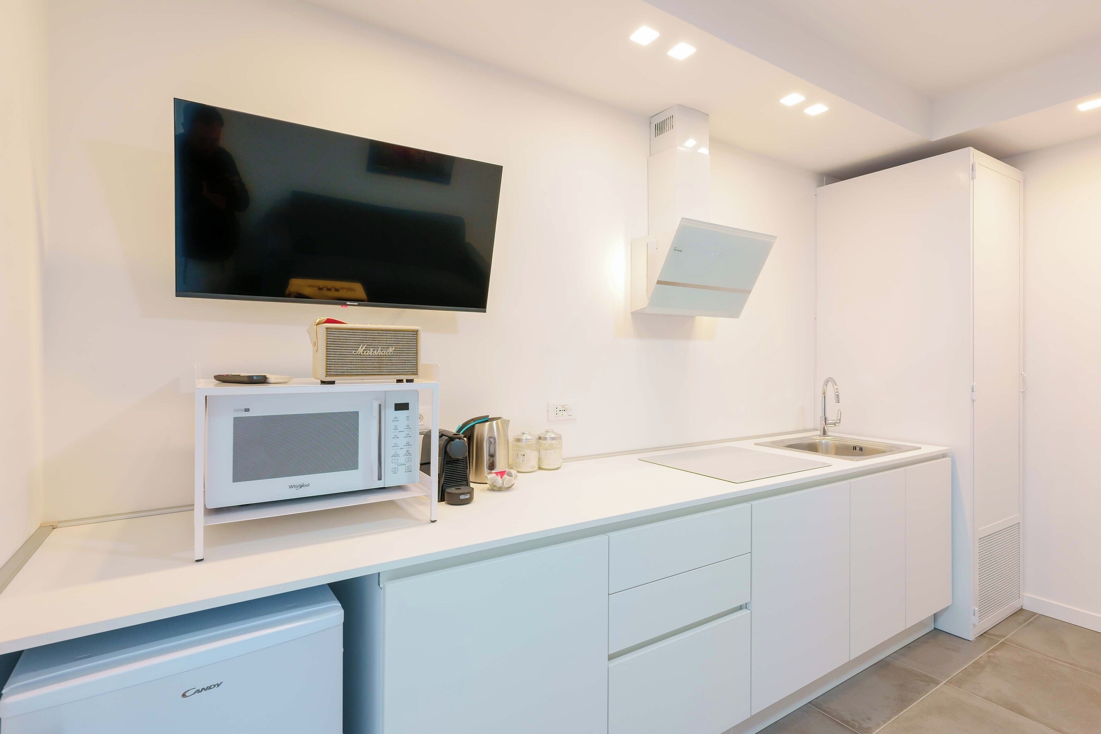 A modern kitchen with a flat-screen TV, microwave, kettle, and sink.
