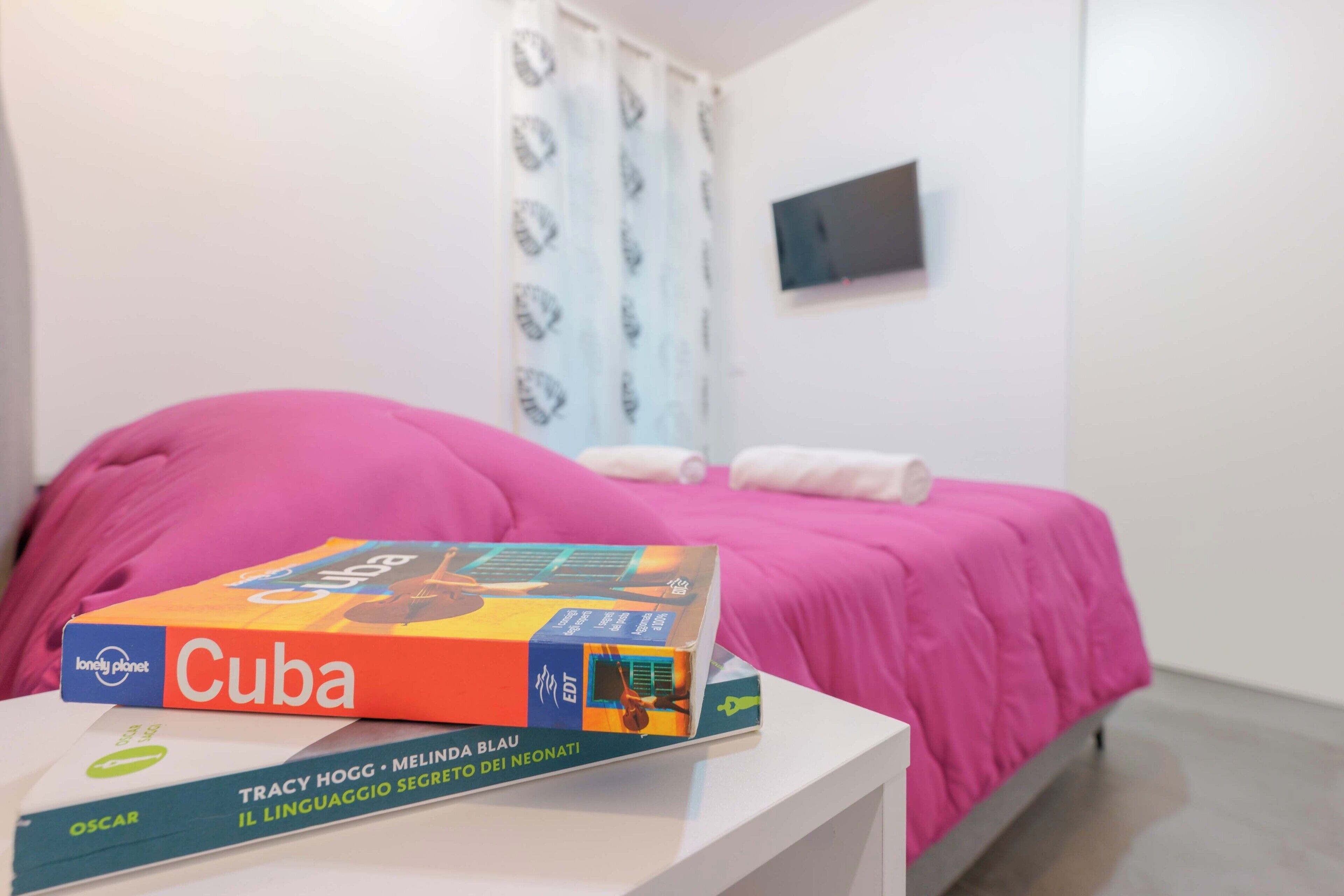 Una cama con cubrerosa, una mesita de noche blanca y un libro titulado 'Cuba' sobre la mesa.