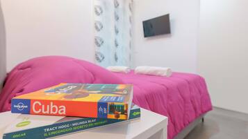 Una cama con cubrerosa, una mesita de noche blanca y un libro titulado 'Cuba' sobre la mesa.