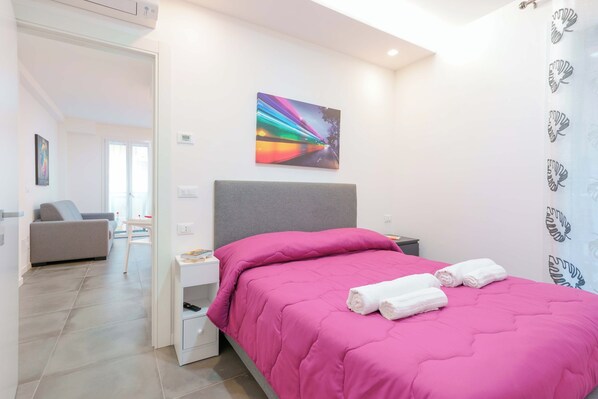 A bedroom with a bed, a nightstand, a grey headboard, a painting on the wall, and a bathroom visible through an open door. - Mascarella Apartments (Bologna)