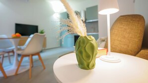 A modern living room with a green vase, a lamp, and a dining area in the background. - Mascarella Apartments (Bologna)
