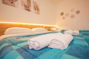 A hotel room with a bed, pillows, a blue and teal bedspread, and rolled white towels.