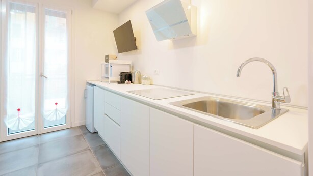 A modern kitchen with a built-in sink, a flat-screen TV, and a sliding glass door leading to an outdoor area. - Mascarella Apartments (Bologna)