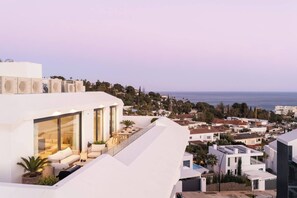 Un bâtiment moderne doté d’une terrasse sur le toit, de grandes fenêtres et offrant une vue sur la mer.