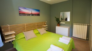 Un dormitorio con una cama, una mesita de noche, un espejo, un radiador y un cuadro de la Torre Eiffel.