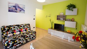 Una sala de estar con sofá, mesa de comedor, televisor y una pared verde con planta.