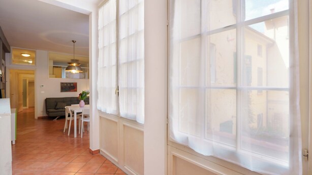 A hallway with a dining area, a sofa, and a window with blinds. - Zamboni 58 Apartment (Bologna)