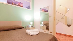A hotel room with a bed, a nightstand with a lamp, a mirror, and a painting on the wall. - Zamboni 58 Apartment (Bologna)