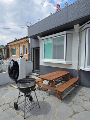 A patio with a barbecue grill and wooden picnic table.
