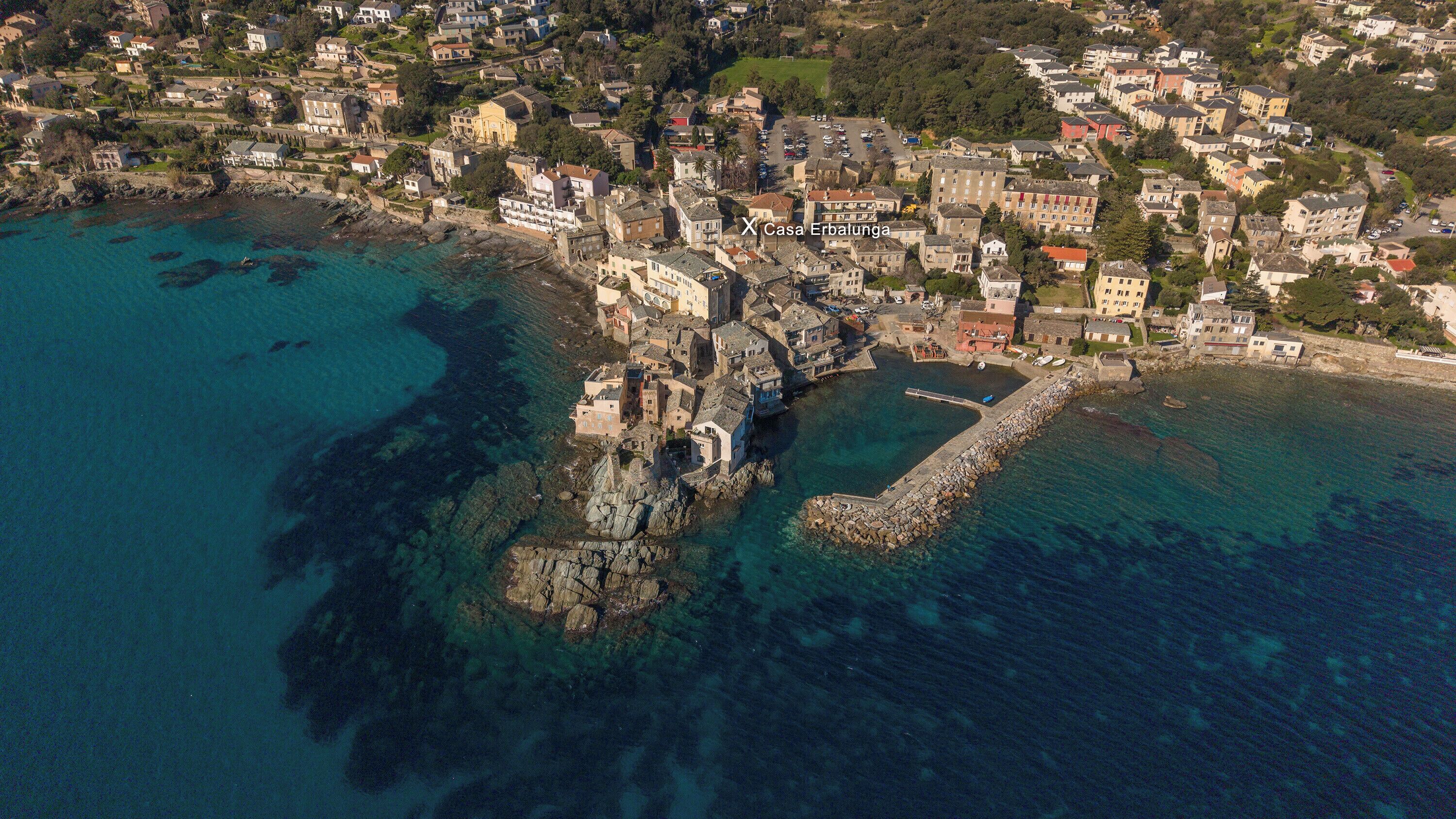 Vue aérienne d’une ville côtière, avec un imposant quai en pierre et des bâtiments le long du littoral.