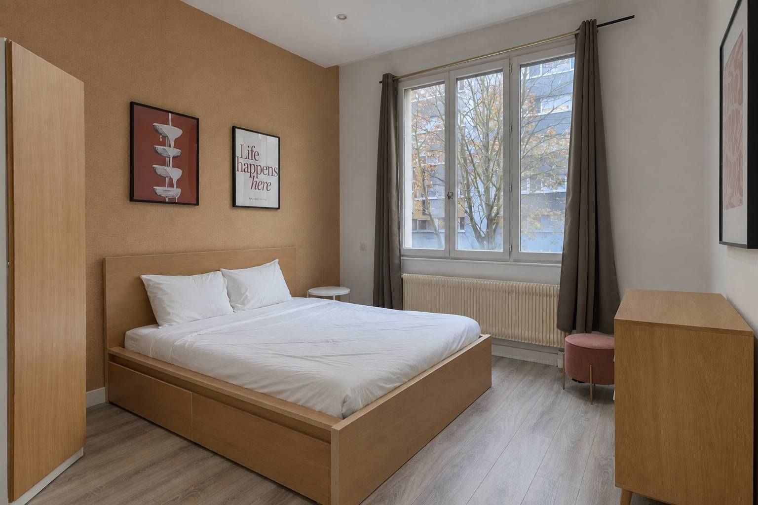 A modern bedroom with a wooden bed, a small bedside table, a radiator, and a window with curtains.