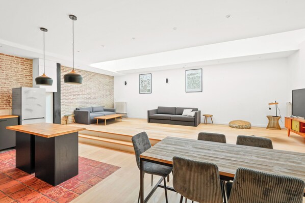 A modern living room with a dining area, a kitchen, and a seating area with a sofa and a TV. - Loft raffiné 3 chambres proche Buttes Chaumont (Paris)